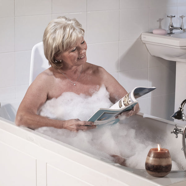 Mangar Archimedes Bath Lift next to bathtub with older woman reading in bubble bath, candle on tub edge, in use view.