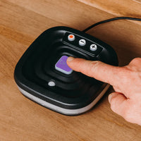 Hand pressing button on Ravencourt Bide Fall Prevention Device for older adults on wooden surface, close-up.