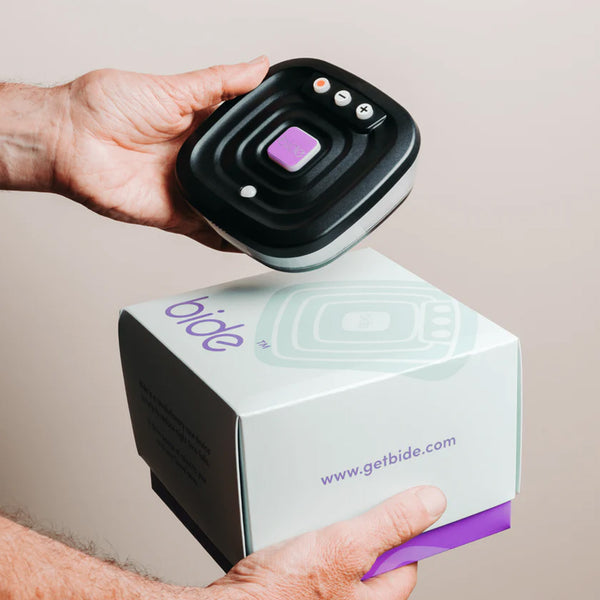 Hands holding a Ravencourt Bide Fall Prevention Device above a bide box for bedside use, close-up.