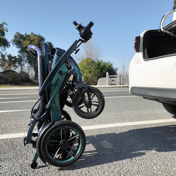 Wizemed C100 carbon fibre folding powerchair upright beside open car boot, outdoors, rear angle.