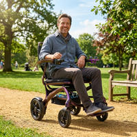 Man using Wizemed C100 carbon fibre folding powerchair on a sunny park path with benches and trees, in use view.