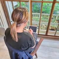 Lifemax Digital Memo Board and Day Date Clock in use on a wooden table near a garden window, rear view.