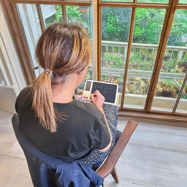 Lifemax Digital Memo Board and Day Date Clock in use on a wooden table near a garden window, rear view.