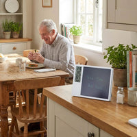 Elderly man eating at table with Lifemax Digital Memo Board and Day Date Clock showing medication reminder, in use.