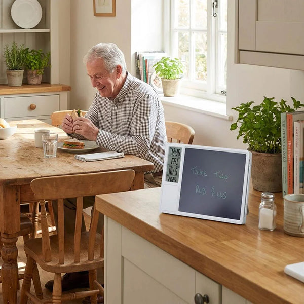Elderly man eating at table with Lifemax Digital Memo Board and Day Date Clock showing medication reminder, in use.