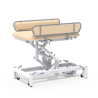 Medi-Plinth electric changing table with metal rails and wheels for wheelchair transfers, NHS-approved, side view.
