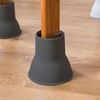 Wooden chair leg fitted with Elephant Feet raiser by Gordon Ellis, two more raised legs in background, close-up view.