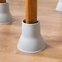Gordon Ellis Elephant Feet raiser supporting a chair leg on a light wood floor, in use close-up.