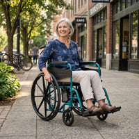 Woman with grey hair using a Days Escape Lite Self Propel Wheelchair on a city pavement with shops and trees, in use view.
