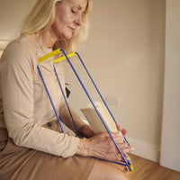 Older woman using Helping Hand Ezy-On Compression Stocking Frame to put on a sock in a bright room with wood flooring, in use.
