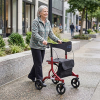 Older woman using Z-Tec Falcon XL Lightweight Rollator walking outside near city shops and greenery, in use view.