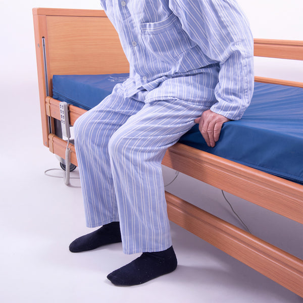 Person in striped pyjamas sitting on Thorpe Mill Firm Edge Mattress with hands resting for support, in use side view.