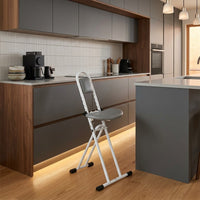 Drive Folding Perching Stool beside a kitchen island, appliances and cabinets in background, room view.