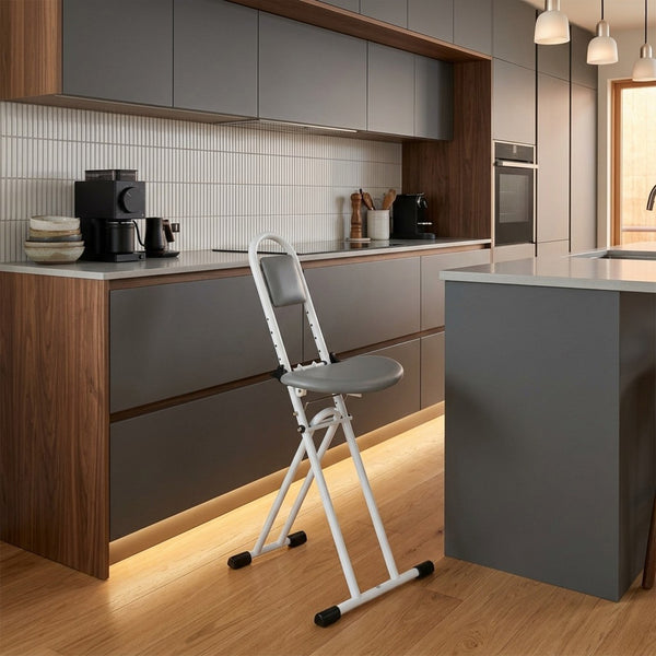 Drive Folding Perching Stool beside a kitchen island, appliances and cabinets in background, room view.