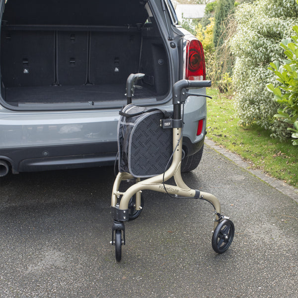 NRS Freestyle 3 Wheel Rollator with black bag behind open SUV boot on driveway next to greenery, rear angle.