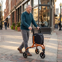 Older man walking outdoors on a brick path with NRS Freestyle 3 Wheel Rollator and black bag attached, in use.