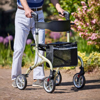 NRS Freestyle 4 Wheel Rollator with mesh storage in use outdoors, greenery and flowers in background, side view.