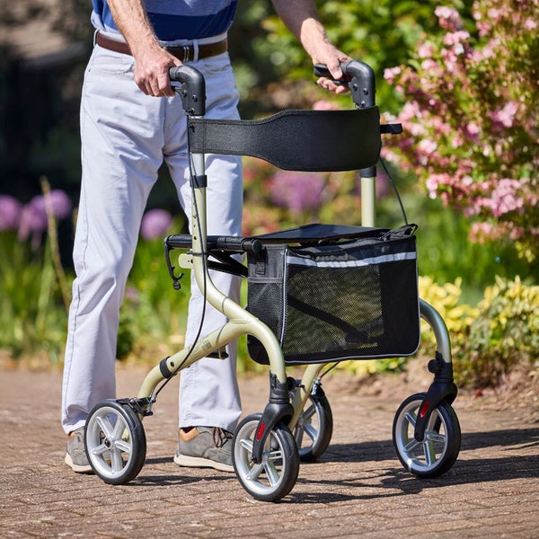 NRS Freestyle 4 Wheel Rollator with mesh storage in use outdoors, greenery and flowers in background, side view.