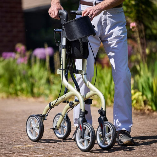 Person using NRS Freestyle 4 Wheel Rollator with bag outdoors among greenery, in use.