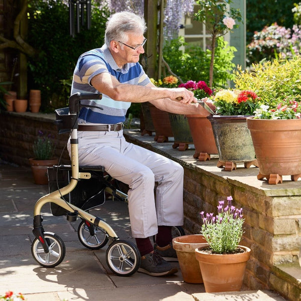 Man sitting on an NRS Freestyle 4 Wheel Rollator tending to potted plants outdoors, in use.