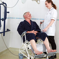 Prism Medical Freeway T80 Reclining Shower Chair in use, elderly man seated with nurse using showerhead, front angle.