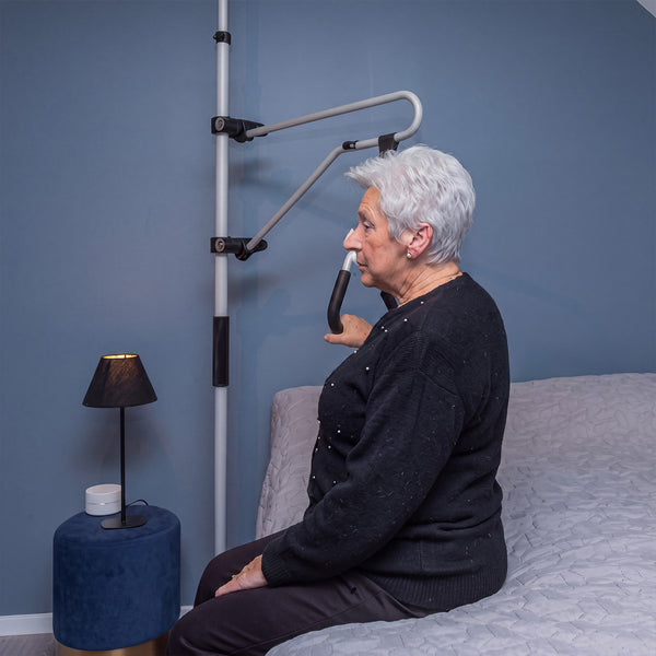 Elderly woman using GRIPO Bed Hoist as a mobility aid while sitting on bed, in use view.