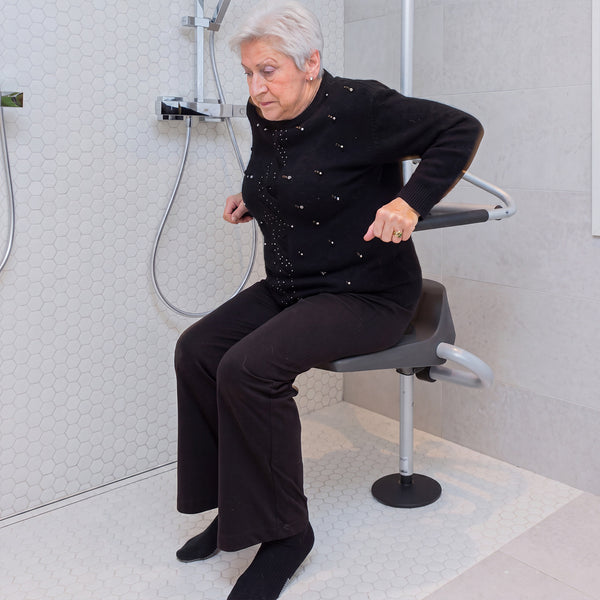 Older woman sitting on GRIPO Collapsible Seat with safety rails and handheld shower, in use.