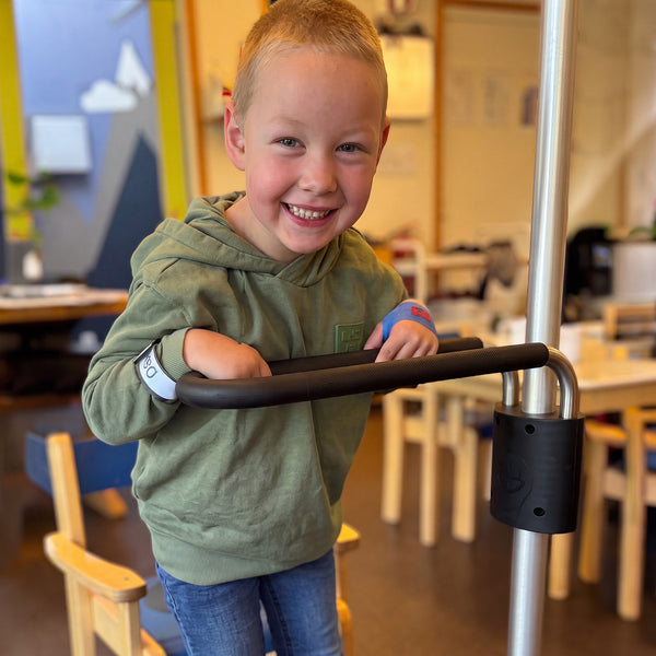 Boy holding GRIPO Multi Grip Support Handle in classroom, chairs in background, product in use, side view.