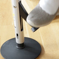 Slipper pressing black pedal on GRIPO Support Pole on wooden floor, close-up in use.