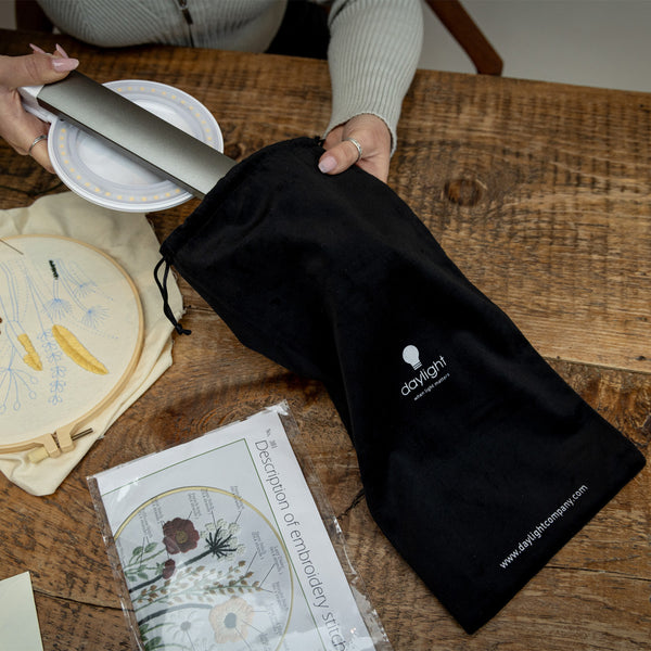 Halo Go 2 Magnifying Lamp by The Daylight Company being packed into a bag, embroidery supplies and hoop close by, in use view.