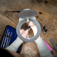 Person using The Daylight Company Halo Go 2 Magnifying Lamp for nail painting, manicure tools and polish on wooden table, in use view.