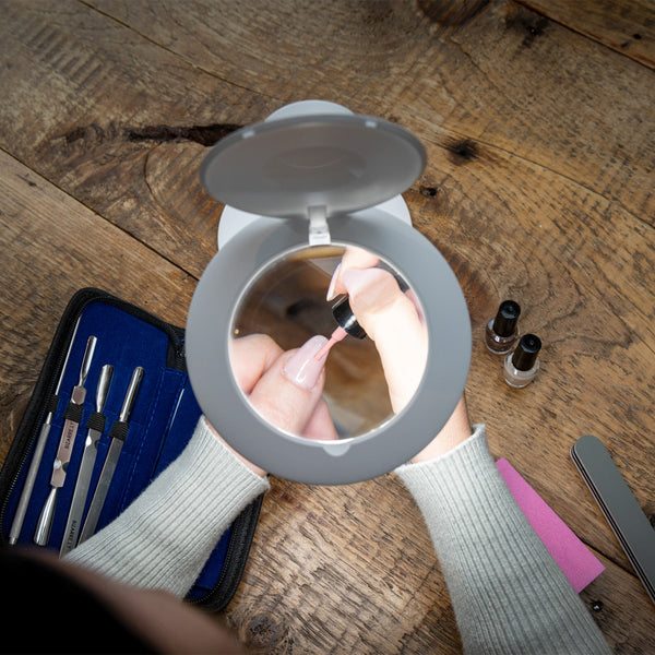 Person using The Daylight Company Halo Go 2 Magnifying Lamp for nail painting, manicure tools and polish on wooden table, in use view.