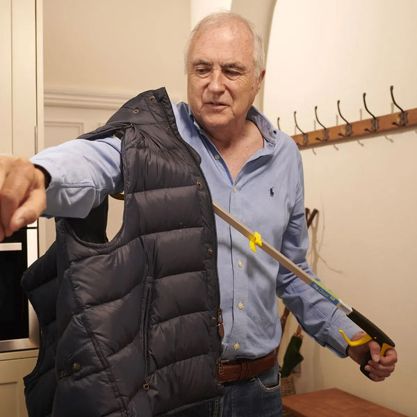 Classic Pro Reacher by Helping Hand used by older man to pick up a vest in hallway with coat hooks, in use view.