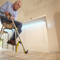 Man using Helping Hand Classic Pro Reacher to pick up an item from the floor in a modern kitchen, in use view.