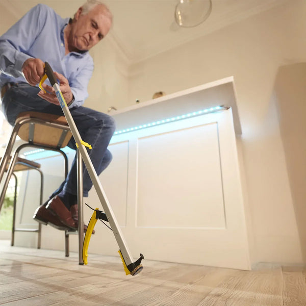 Man using Helping Hand Classic Pro Reacher to pick up an item from the floor in a modern kitchen, in use view.