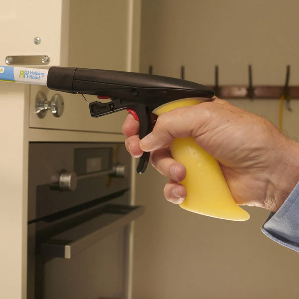 Hand using a Helping Hand Handi-Grip Max to reach a kitchen cabinet by an oven, in use angle.