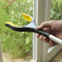 Hand holding a Helping Hand Handi-Grip Max by a glass door, green garden visible outside, in use angle.