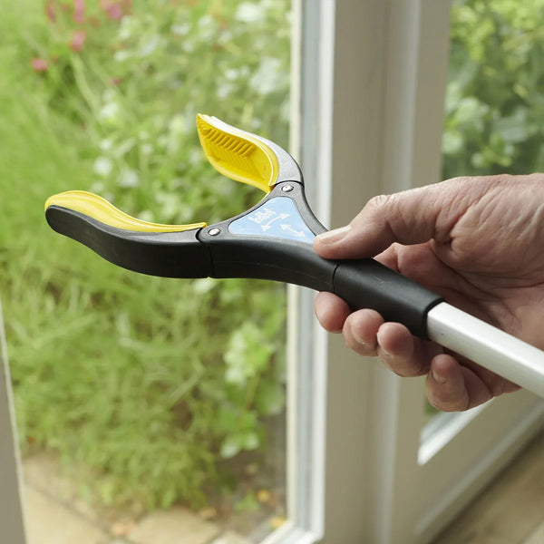 Helping Hand Handi-Grip Pro being used to pick up an item near a glass door, greenery visible outside, in use view.