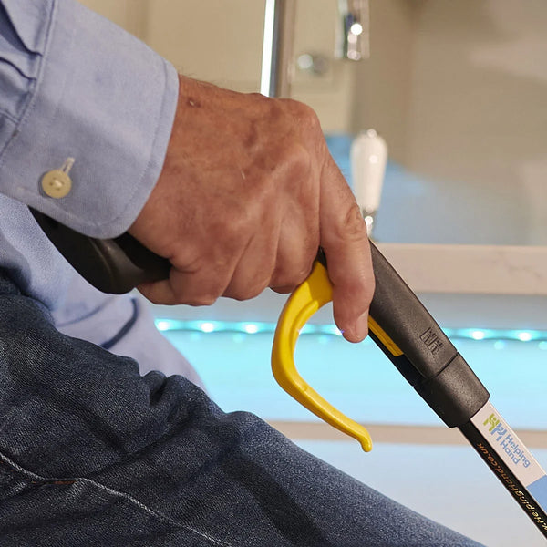 Person using Helping Hand Handi-Grip Pro reaching aid to pick up an item while seated, close-up.