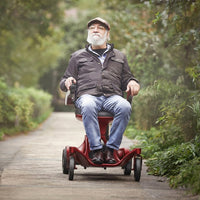 Older man using Urathon Hero Carbon Fibre Powerchair on a garden path, greenery in background, in use view.