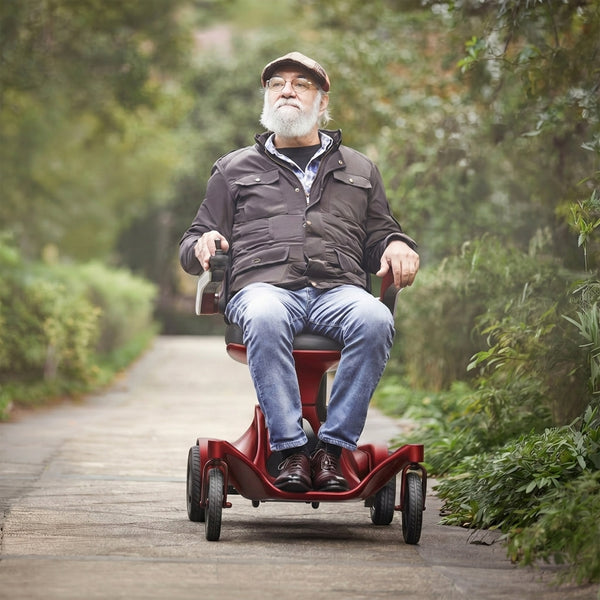 Older man using Urathon Hero Carbon Fibre Powerchair on a garden path, greenery in background, in use view.