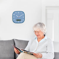 Lifemax High Contrast Day-Date Wall Clock on wall behind older woman reading magazine on sofa, in use view.