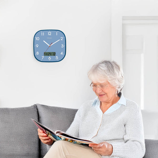 Lifemax High Contrast Day-Date Wall Clock on wall behind older woman reading magazine on sofa, in use view.
