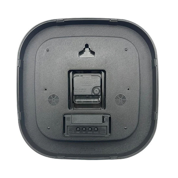 Robotic vacuum next to a Lifemax High Contrast Day-Date Wall Clock, battery compartment and openings visible, top angle.