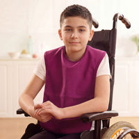 Boy in wheelchair wearing Care Designs Junior Tabard Style Bib, machine washable, sitting indoors, neutral expression, front view.