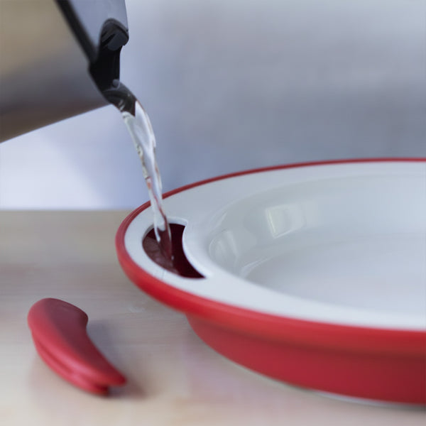 Hot water poured from a kettle into an ORNAMIN Keep Warm Plate on a light surface, in use view.