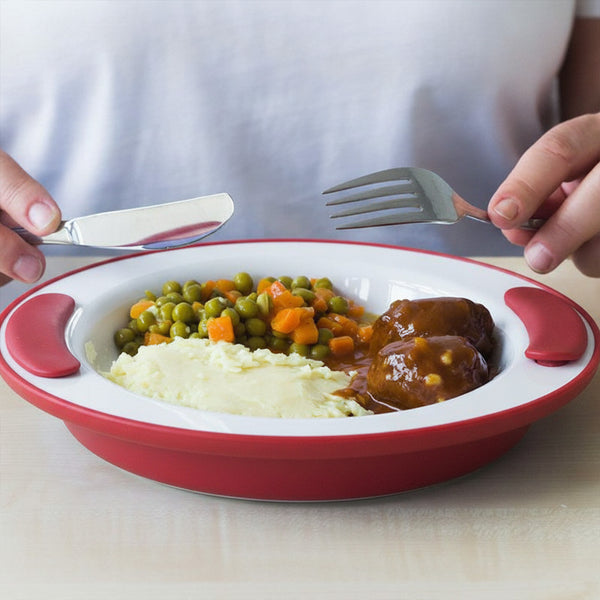 Person holding fork and knife over ORNAMIN Keep Warm Plate with mashed potatoes, peas, carrots, and meat in sauce in use.