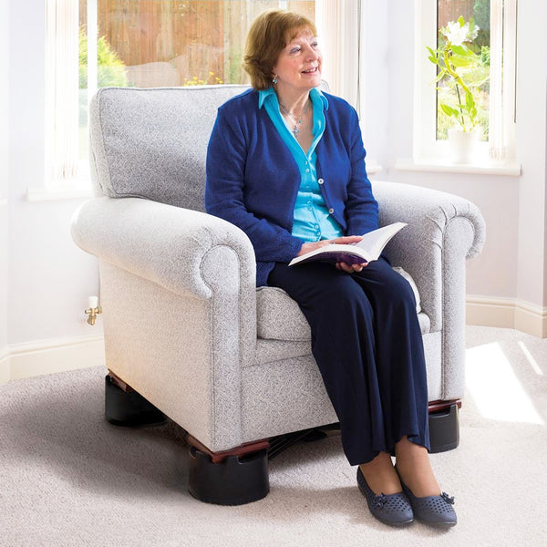 Older woman sits reading in sunlight with Langham Multi Purpose Raiser Chair Kit fitted to a chair, in use side view.