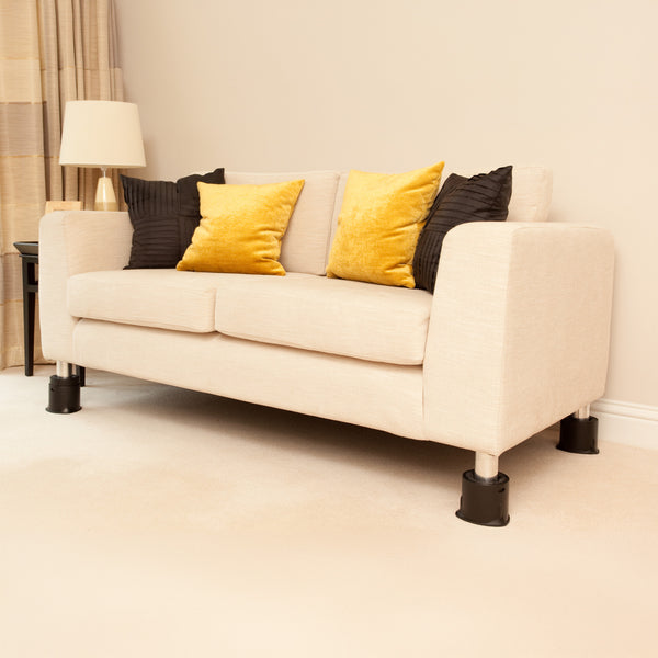 Sofa with yellow and black cushions on Langham SureGrip Furniture Raisers in a bright room with lamp and curtains, front view.