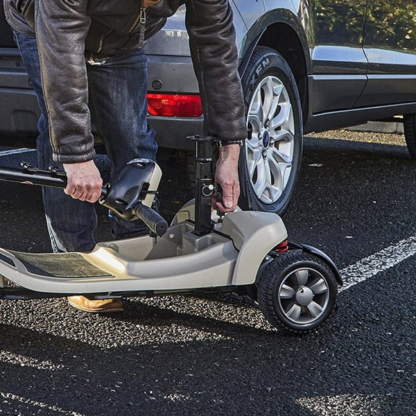 Person adjusting Motion Healthcare Lithilite Scooter with puncture proof wheels next to parked car in parking area, side view.